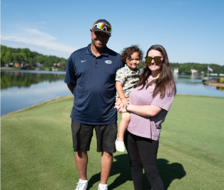 woman holding boy in front of man on golf course