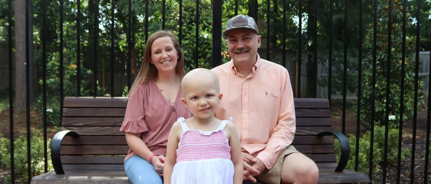 girl standing in front of parents sitting on bench
