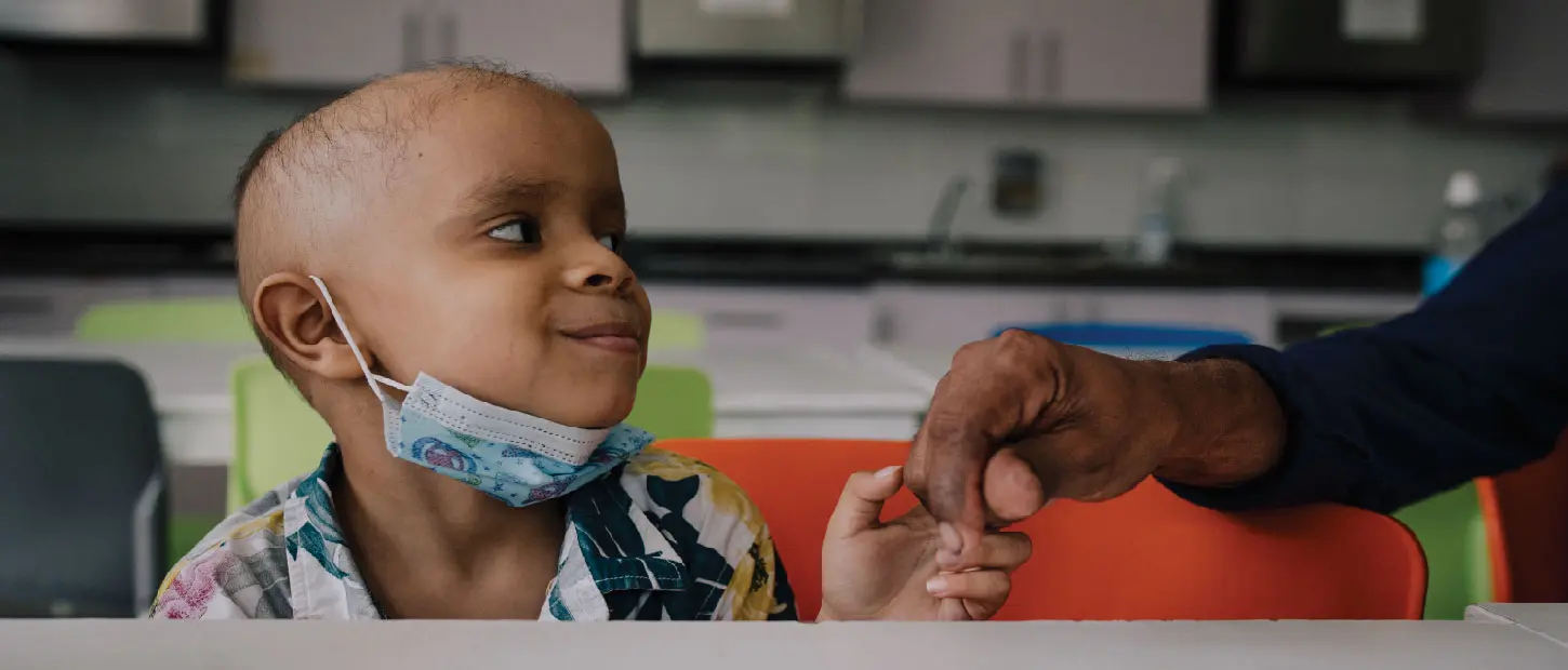 boy holding hand smiling with a mask on
