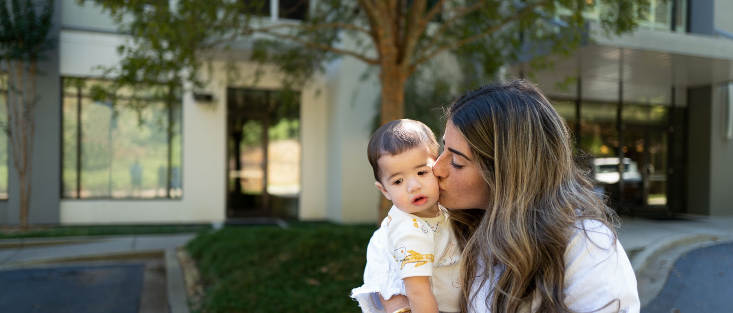woman kissing baby in front of house