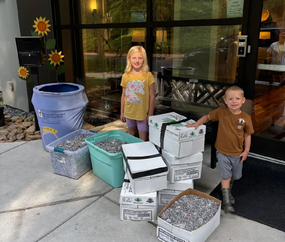 girl and boy standing with bins of pop tabs