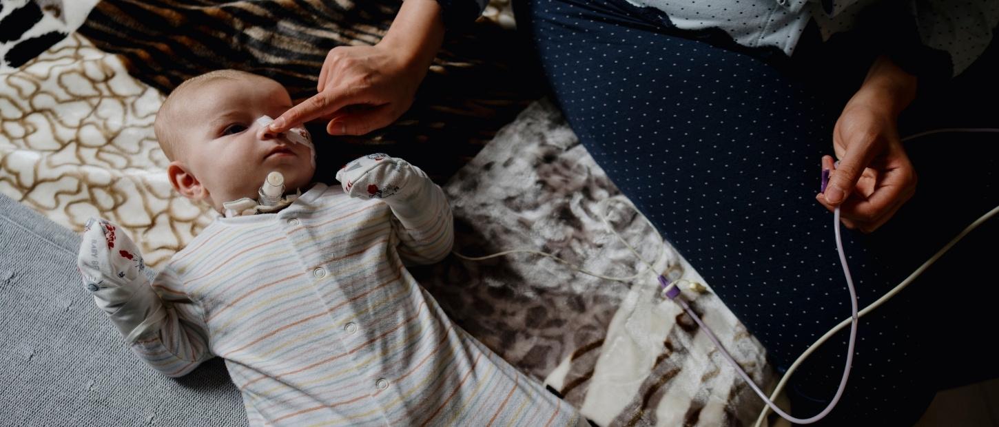 baby laying on bed with woman touching its nose