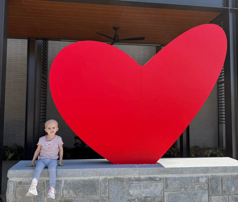 girl sitting beside heart sculpture